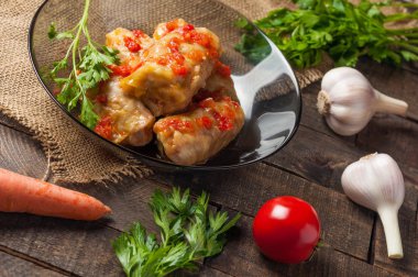 Çuvallama ve rustik ahşap masa üzerinde sebze yakın siyah cam tabakta pirinç ve et dolu domates soslu haşlanmış lahana rulo bir porsiyon