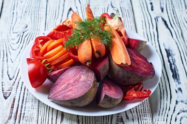 Yuvarlak seramik tabakta taze taze sebzeler yığını mutfaktaki eski, beyaz ahşap masa üzerinde yatıyor. Sağlıklı gıda konsepti