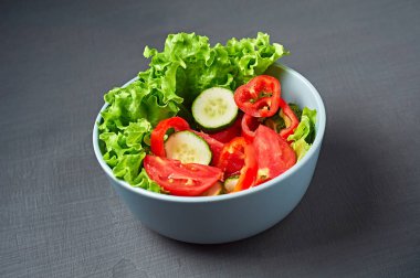 Dolu bir kase düşük kalorili salata, domates, biber, salatalık çizik koyu betonda yatıyor. Vejetaryen, diyet, sağlıklı yiyecekler. Yakın plan.
