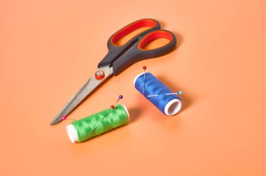 Atölyedeki turuncu terzi masasında renkli iplik ve iğnelerle aksesuar, makas ve makaralar dikmek. Yakın plan.