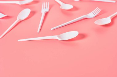 Pembe arka plana saçılmış tek kullanımlık beyaz kaşıklar ve çatallar. Çevreyi, ekolojiyi, piknik, parti ve diğer etkinlikleri kurtarma kavramı. Boşluğu kopyala