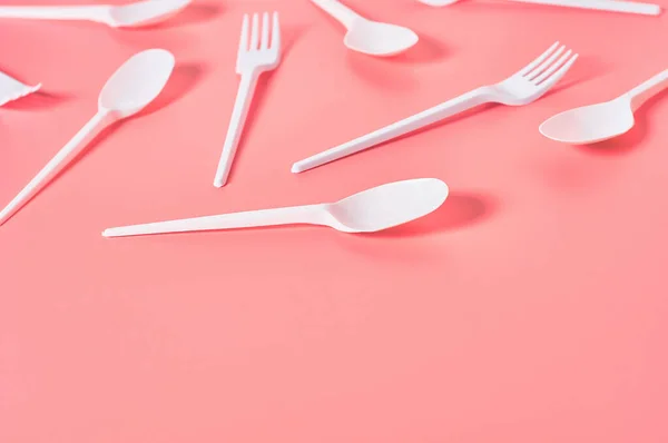 ピンクの背景に散在する白い使い捨てスプーンとフォーク 生態系 ピクニック パーティーなどのイベントでのレクリエーションの概念 スペースのコピー — ストック写真
