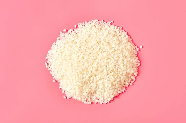 Heap of grain of white rice on pink background. Top view