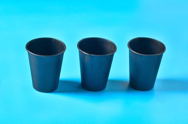 Mavi arka planda sıcak içecekler için üç sıra dağınık siyah karton bardak. Çevre koruma kavramı, kahve molası, ekoloji, çöp geri dönüşümü