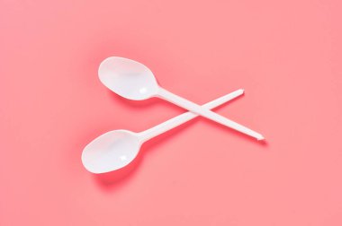 Pembe arka plana saçılmış iki tek kullanımlık kaşık. Çevreyi, ekolojiyi, piknik, parti ve diğer etkinlikleri kurtarma kavramı. Üst görünüm