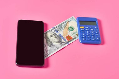 Akıllı telefon, hesap makinesi ve pembe arka planda dolar banknotu. Mobil bankacılık kavramı. Evden online alışveriş. Uzaklık denetimi mali denge