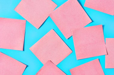 Mavi arka planda bir sürü pembe kare boş kağıt çıkartması vardı. Uzayı kopyala Üst görünüm