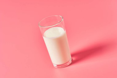 Pembe arka planda bir bardak taze süt.