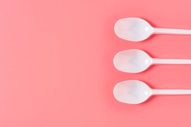 Pembe arka plana saçılmış tek kullanımlık beyaz kaşıklar. Çevreyi, ekolojiyi, piknik, parti ve diğer etkinlikleri kurtarma kavramı. Uzayı kopyala Üst görünüm