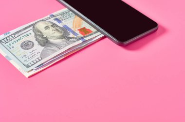Akıllı telefon ve pembe arka planda dolar banknotu. Mobil bankacılık kavramı. Evden online alışveriş. Uzaklık denetimi mali denge