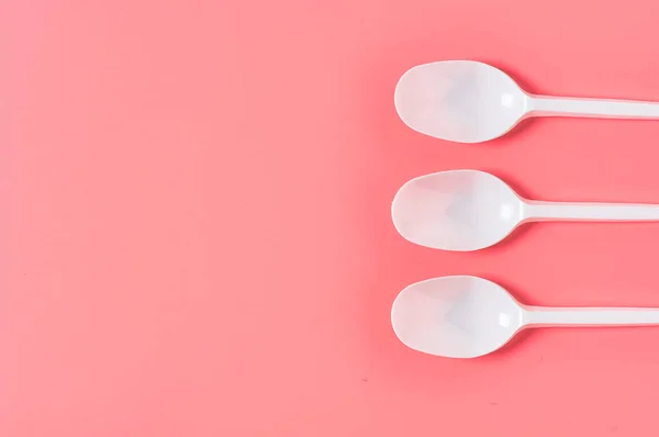 Row of white disposable spoons scattered on pink background. Concept of save environment, ecology, recreation on picnic, party and other events. Copy space. Top view