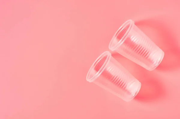 Disposable plastic glasses scattered on pink background. Concept of save environment, ecology, recreation on picnic, party and other events. Copy space. Top view