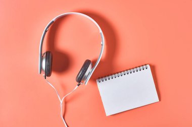 Kablolu, turuncu arka planda boş kağıt defter olan modern beyaz kulaklıklar. Müzik konsepti. Uzayı kopyala Üst görünüm