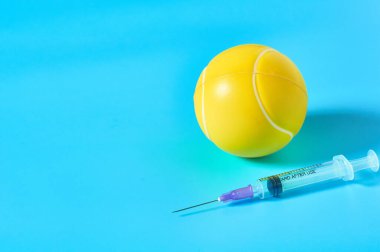 Mavi arka planda şırınganın yanında tenis topu var. Profesyonel sporda doping kavramı. Rehabilitasyon, yarışmadan sonra tedavi. Turnuvada kullanılan yasadışı ilaçlar