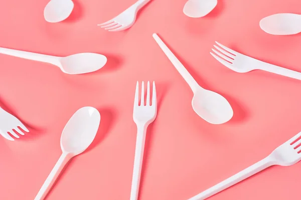 White disposable spoons and forks scattered on pink background. Concept of save environment, ecology, recreation on picnic, party and other events