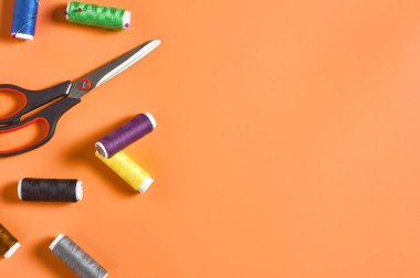 Atölyedeki turuncu terzi masasında renkli iplik ve iğnelerle aksesuar, makas ve makaralar dikmek. Mesaj için yer var. Üst görünüm