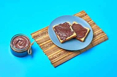 Tabakta vanilyalı ekmeğin yanında erimiş çikolata ya da kremalı cam kavanoz ve mutfaktaki mavi masanın üzerinde bambu hasırı var. Besleyici kahvaltı ya da öğle yemeği kavramı