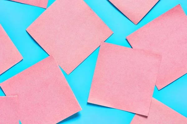 Mavi arka planda bir sürü pembe kare boş kağıt çıkartması vardı. Uzayı kopyala Üst görünüm