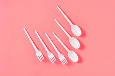 Tek kullanımlık beyaz kaşık ve çatal pembe arka plana saçılmış. Çevreyi, ekolojiyi, piknik, parti ve diğer etkinlikleri kurtarma kavramı. Üst görünüm