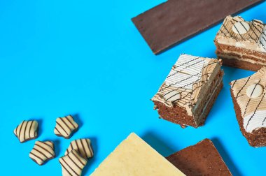 Farklı çikolata ve şekerlemelerin yanında üç dikdörtgen pasta partideki mavi masada duruyor. Kutlama konsepti. Metin için boşluk