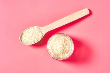 Cam kavanoz ve pembe arka planda ahşap kaşık pirinç taneleri. Üst görünüm