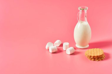 Bir sürahi taze süt, yoğurt ya da ince waffle 'ların yanında kefir ve pembe arka planda lokum. Metin için boşluk