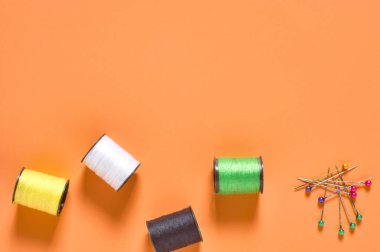 Atölyedeki turuncu terzilerin masasına renkli ipliklerle saçılmış iğne ve makaralar. Mesaj için yer var. Üst görünüm