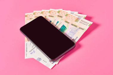 Pembe arka planda akıllı telefon ve Ukrayna parası. Mobil bankacılık kavramı. Evden online alışveriş. Uzaklık denetimi mali denge