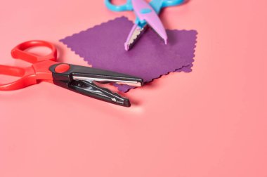 Dekoratif kıvırcık kesim için iki makas. Pembe zemin üzerinde dalga sınırı olan el sanatları için de boş kağıt. El yapımı, boş zaman ve anaokulu eğitimi kavramı