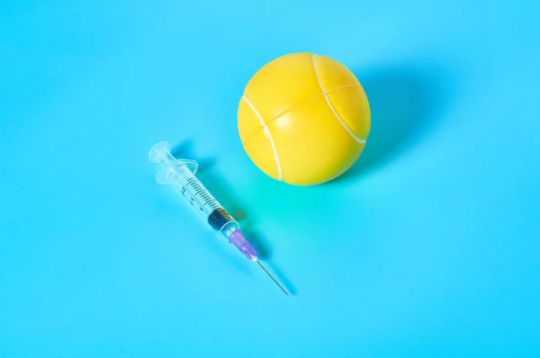 Tennis ball near syringe on blue background. Concept of doping in professional sport. Rehabilitation, treatment after competition. Illegal medicaments using on tournament