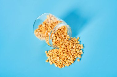 Mavi arka planda cam kavanozdan kurumuş bezelye taneleri döküldü.