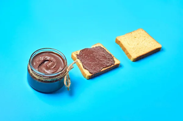 バニラパンの近くに溶かしたチョコレートでいっぱいのガラス瓶はキッチンの青い机の上にあります 栄養価の高い朝食 ランチのコンセプト — ストック写真