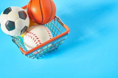 Mavi arka planda metal market sepetinde farklı toplar. Spor aksesuarları alıyorum. Sporda yolsuzluk kavramı