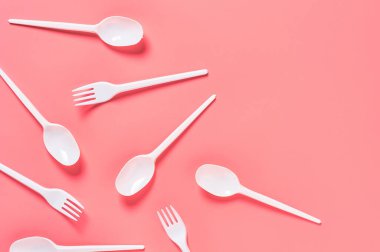 Pembe arka plana saçılmış tek kullanımlık beyaz kaşıklar ve çatallar. Çevreyi, ekolojiyi, piknik, parti ve diğer etkinlikleri kurtarma kavramı. Üst Manzara. Boşluğu kopyala