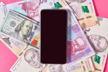 Akıllı telefon ve pembe arka planda farklı paralar. Mobil bankacılık kavramı. Evden online alışveriş. Uzaklık denetimi mali denge