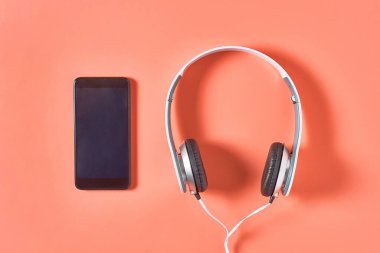Akıllı telefonun yanında kablo olan modern beyaz kulaklıklar ya da turuncu arka planda tablet. Çağrı merkezi konsepti. Üst görünüm