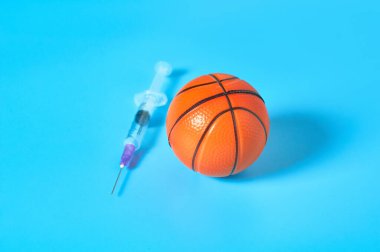 Mavi arka planda şırınganın yanında basketbol topu. Profesyonel sporda doping kavramı. Rehabilitasyon, yarışmadan sonra tedavi. Turnuvada kullanılan yasadışı ilaçlar