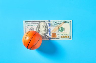 Basketbol topu ve mavi arka planda 100 dolarlık banknot. Spor aksesuarları alıyorum. Sporda yolsuzluk kavramı