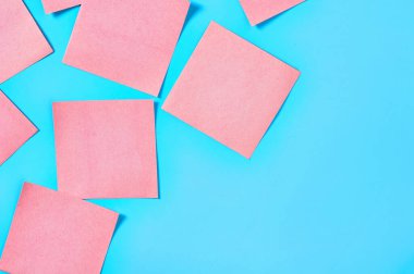 Mavi arka planda bir sürü pembe kare boş kağıt çıkartması vardı. Uzayı kopyala Üst görünüm