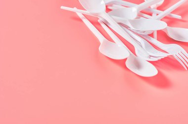Pembe arka planda tek kullanımlık beyaz kaşık ve çatal yığını. Çevreyi, ekolojiyi, piknik, parti ve diğer etkinlikleri kurtarma kavramı. Boşluğu kopyala