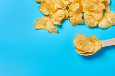 Baharatlı patates cipsi ve mavi arka planda ahşap kaşık. Metin için boşluk