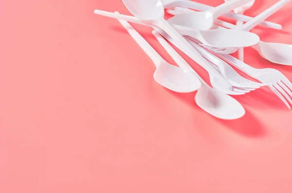 Heap of white disposable spoon and fork on pink background. Concept of save environment, ecology, recreation on picnic, party and other events. Copy space
