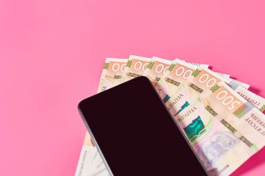 Pembe arka planda akıllı telefon ve Ukrayna parası. Mobil bankacılık kavramı. Evden online alışveriş. Uzaklık denetimi mali denge