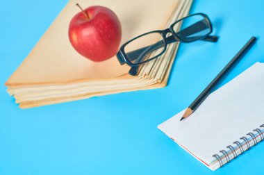 Bir yığın boş dergi, gazete ya da bazı belgeler ve kırmızı elma, not defteri, kalem, mavi masadaki gözlükler. İş, eğitim ya da okula dönüş kavramı. Gazeteci ya da sekreterin işyeri