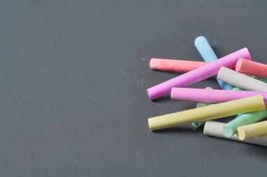Siyah karatahtanın üzerinde bir sürü renkli tebeşir parçası. Boşluğu kopyala
