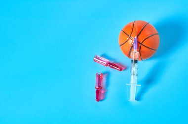 Şırınganın yanında basketbol topu ve mavi arka planda ampul. Profesyonel sporda doping kavramı. Rehabilitasyon, yarışmadan sonra tedavi. Turnuvada kullanılan yasadışı ilaçlar