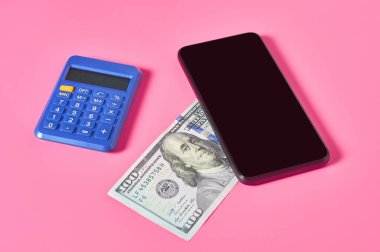 Akıllı telefon, hesap makinesi ve pembe arka planda dolar banknotu. Mobil bankacılık kavramı. Evden online alışveriş. Uzaklık denetimi mali denge