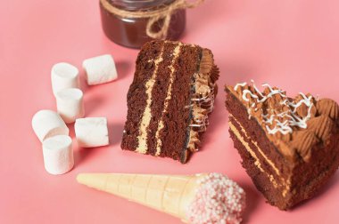 Farklı tatlıların yanında çikolatalı kek parçaları pembe masanın üzerinde yatıyor. Yakın plan.