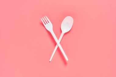 Pembe arka planda tek kullanımlık beyaz kaşık ve çatal. Çevreyi, ekolojiyi, piknik, parti ve diğer etkinlikleri kurtarma kavramı. Üst görünüm