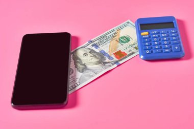 Akıllı telefon, hesap makinesi ve pembe arka planda dolar banknotu. Mobil bankacılık kavramı. Evden online alışveriş. Uzaklık denetimi mali denge